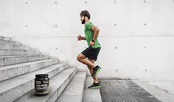 Male athlete running up stairs outside with bottle of whey protein