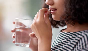 Woman taking vitamin or supplement with glass of water