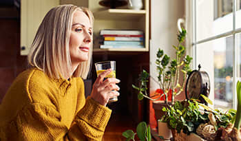 Mature woman drinking glass of water by window with lemon