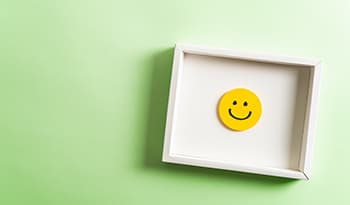 Happy yellow smiling emoticon face frame hanging on green background