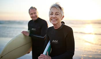 Mature woman and man smile on the beach with surfboards