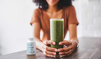 Woman sitting at table with green smoothie and bottle of detox support supplements