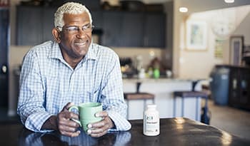Mature man drinking coffee at home with stress supplement bottle on table