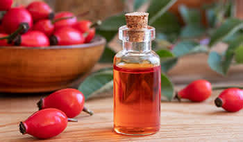 Rosehip oil in glass bottle on table with rosehip buds 