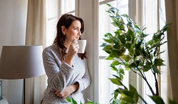 Brunette woman drinking coffee in the morning looking out the window