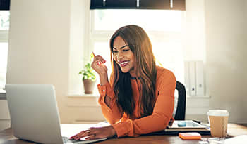 Young smiling woman in orange shirt sitting at her desk looking at a computer 