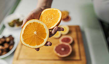 Female hand holding fresh orange in her kitchen above cutting board with slices of fruit