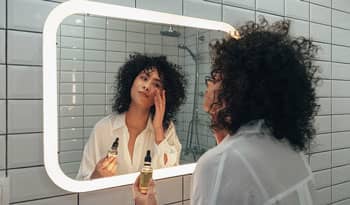 woman applying bakuchiol serum in her bathroom mirror