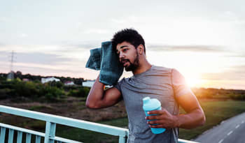 Male athlete wiping head with towel taking a break after a workout holding a shaker bottle