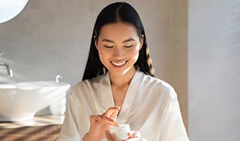 Asian woman applying skincare product in bathroom
