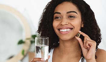 Woman with healthy skin and hair taking fish oil supplement with water