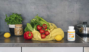 Fresh fruit and vegetables like celery, peppers, tomatoes, lemon, and vitamin C supplement on kitche
