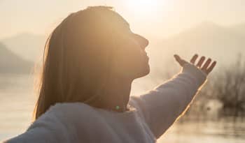 woman standing with arms outstretched as sun shines on her
