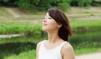 Asian woman taking deep breath outside