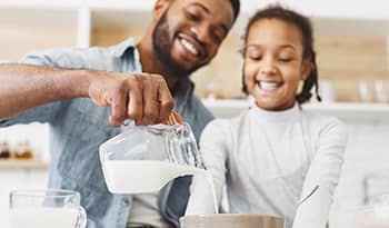 Young dad and daughter pouring milk into cereal for breakfast