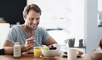 Man eating healthy breakfast with cholesterol support supplement on table