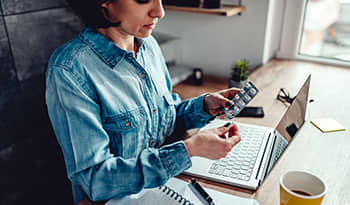 Young brunette woman in jean shirt sitting at desk taking a daily supplement 