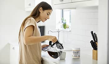 Woman pouring coffee with collagen supplement on kitchen counter