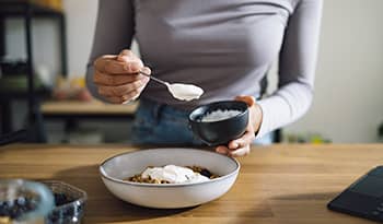 Woman making yogurt and oatmeal bowl in kitchen