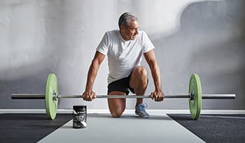 Mature male strength training with barbell in the gym