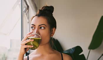 Healthy woman drinking green juice by the window
