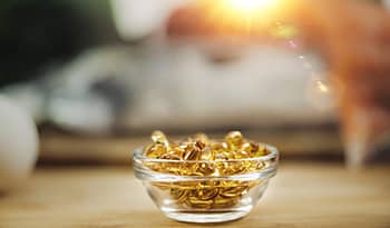Fish oil supplements in glass bowl on table with sun in the background