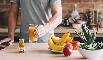 Man drinking fresh juice in kitchen with turmeric and fruits