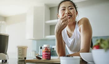 Healthy woman eating breakfast in her kitchen with yogurt and fiber supplement on counter
