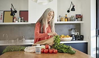 Healthy mature woman unpacking groceries in kitchen