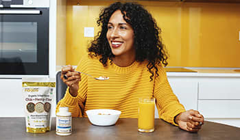 Healthy woman eating breakfast in kitchen with flaxseeds and omega-3 supplement on table