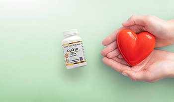 Hands holding red ceramic heart on green background with CoQ10 supplement