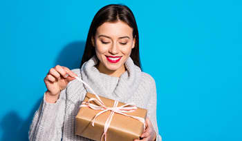 woman against blue background opening a wrapped gift