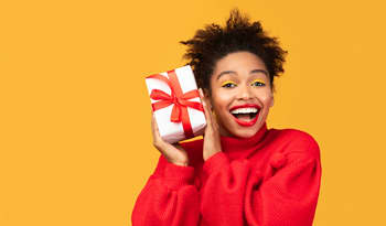 woman against yellow background holding up an unopened self-care gift