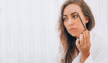 celebrity makeup artist in a white bathrobe applying a brow pencil to her eyebrow