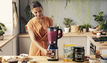 Healthy woman making smoothie in bright kitchen with spirulina, protien powder, and berries