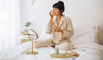 woman sitting on bed applying clean beauty products to her face