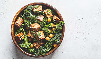 Teriyaki tofu salad with kale and chickpeas in a wooden bowl on white background
