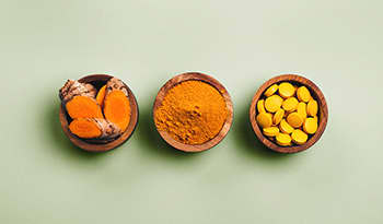 Turmeric in wooden bowls, fresh turmeric root, powdered, pills on green background