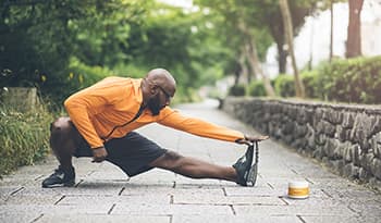 Athletic male stretching outside for a run with electrolyte bottle on ground