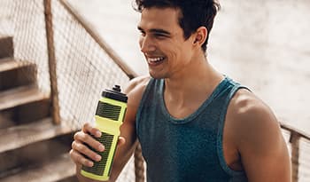 Young athletic male taking break from workout to drink from water bottle