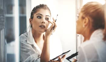 woman applying eyeshadow in mirror using eyeshadow palette dupe