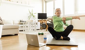 Elderly woman doing yoga video stretching at home on yoga mat