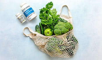 Green vegetables in reusable bag on table with supplements