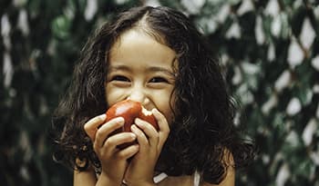 Little girl with curly hair eating a red apple