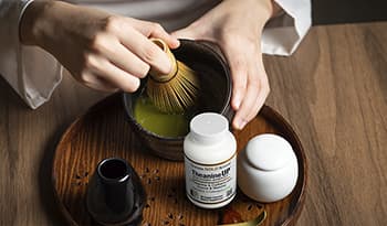 Making traditional matcha in bowl with wooden whisk with theanine supplement on table