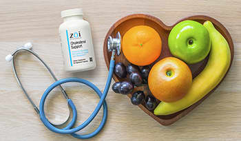 Fruit in heart shaped bowl, stethoscope, and cholesterol support supplement on wood table