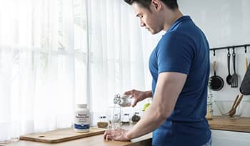 Fit male pouring glass of water with magnesium supplement bottle on counter