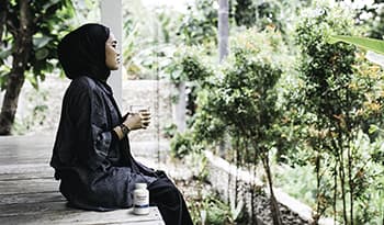 Young woman sitting in backyard looking at trees holding glass of water with magnesium supplement
