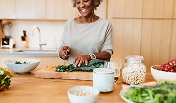 Mature woman preparing healthy kale vegetable salad in kitchen