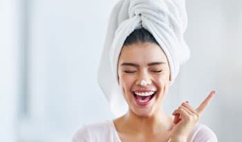 woman smiling with eyes closed and hair up in a towel with a dab of collagen cream on her nose